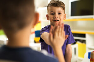 Happy boy giving high five to his friend at preschool.