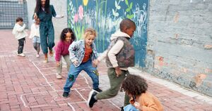 A group of children and their teacher play hopscotch outside.
