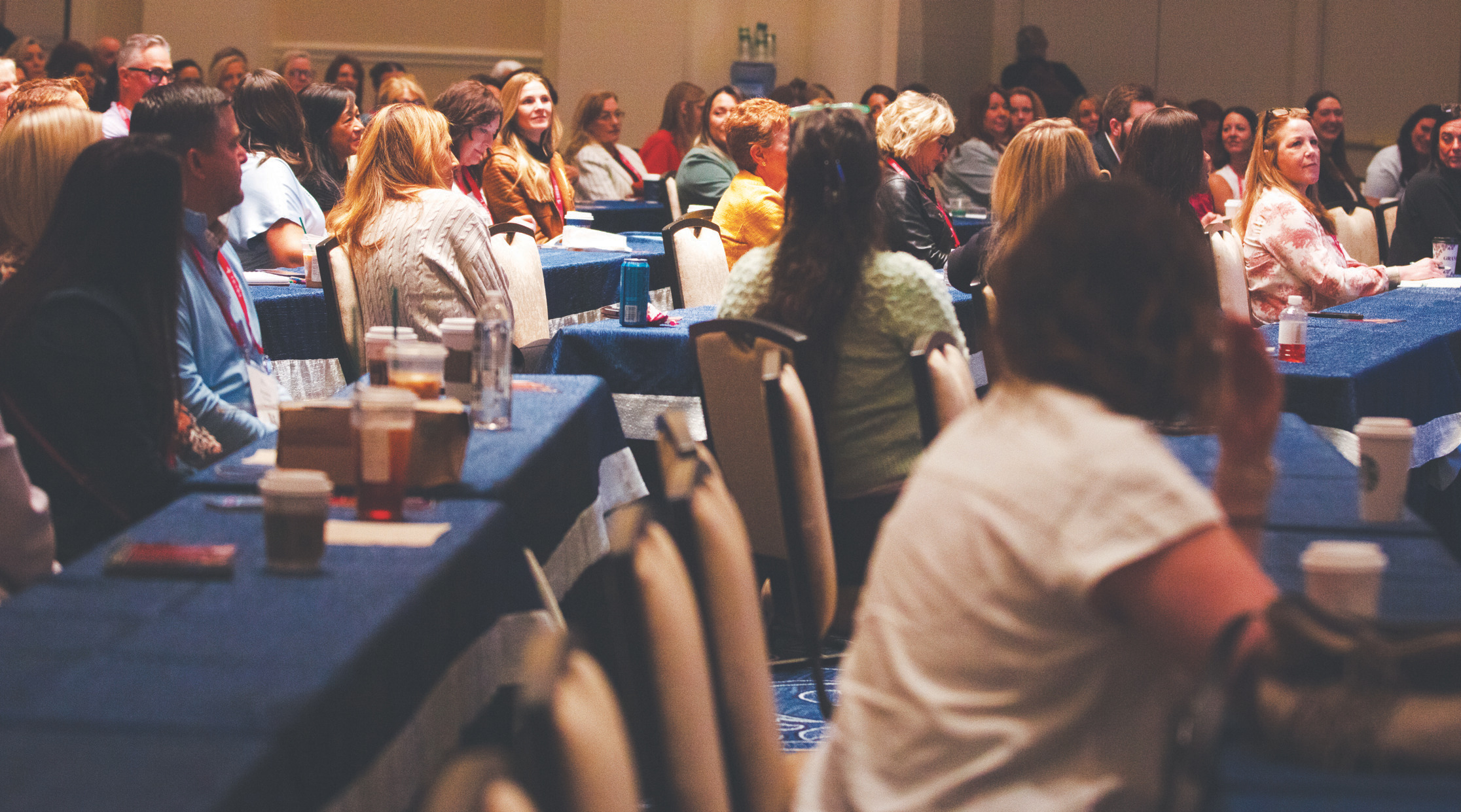 Conference attendees seated at rows of tables listening to a session