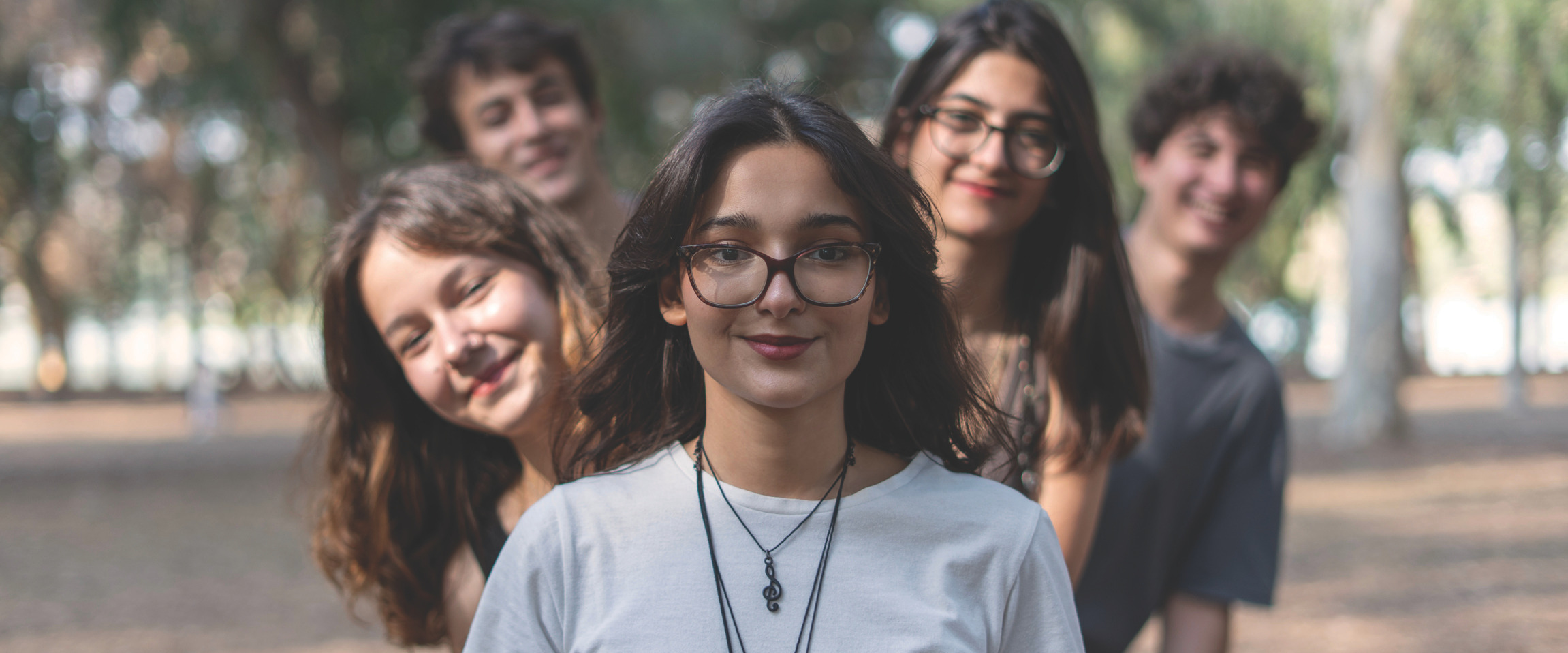 Group of smiling young adults standing outdoors in a park, posing for a photo.