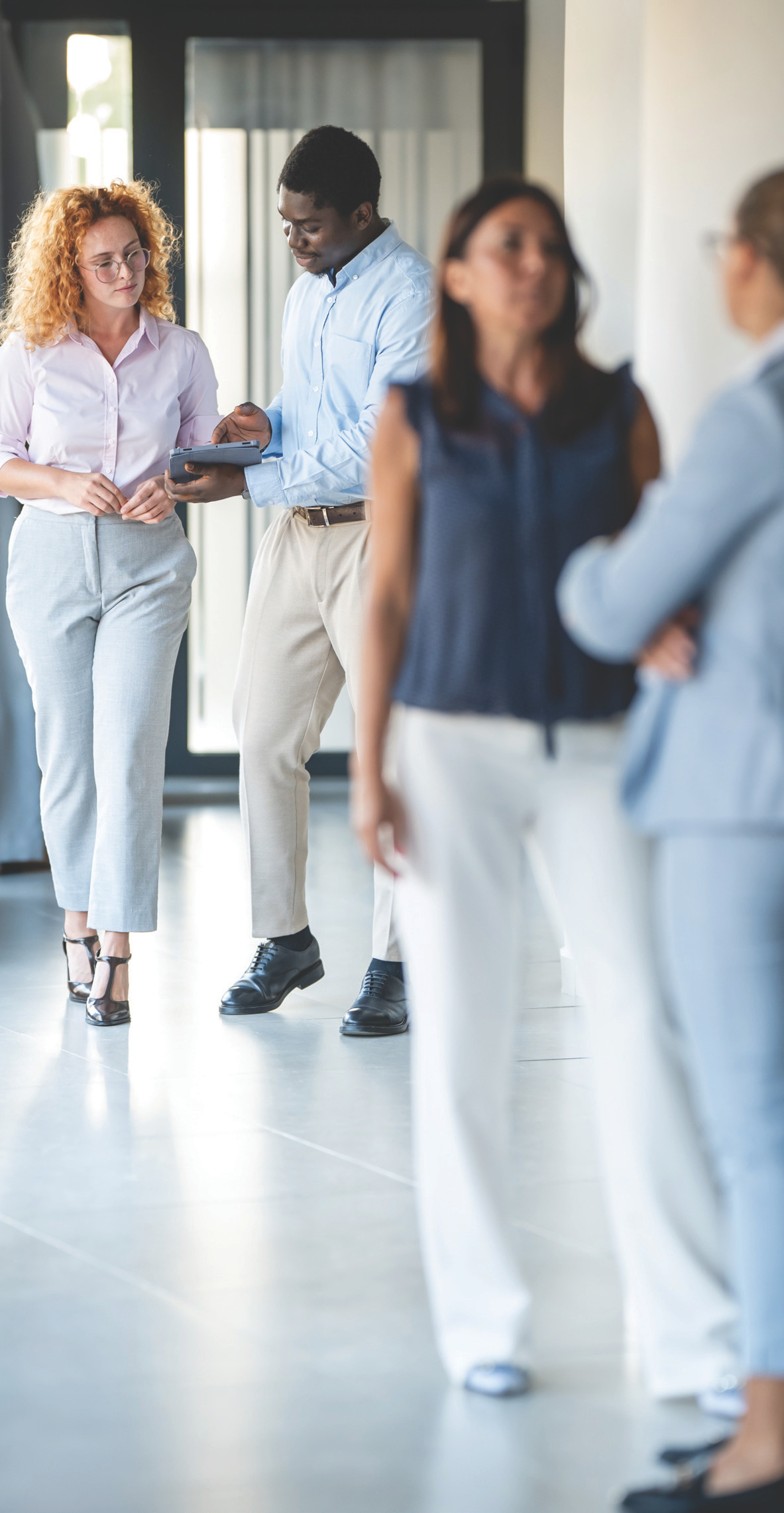 Professionals walking and talking in a bright hallway, dressed business-casual