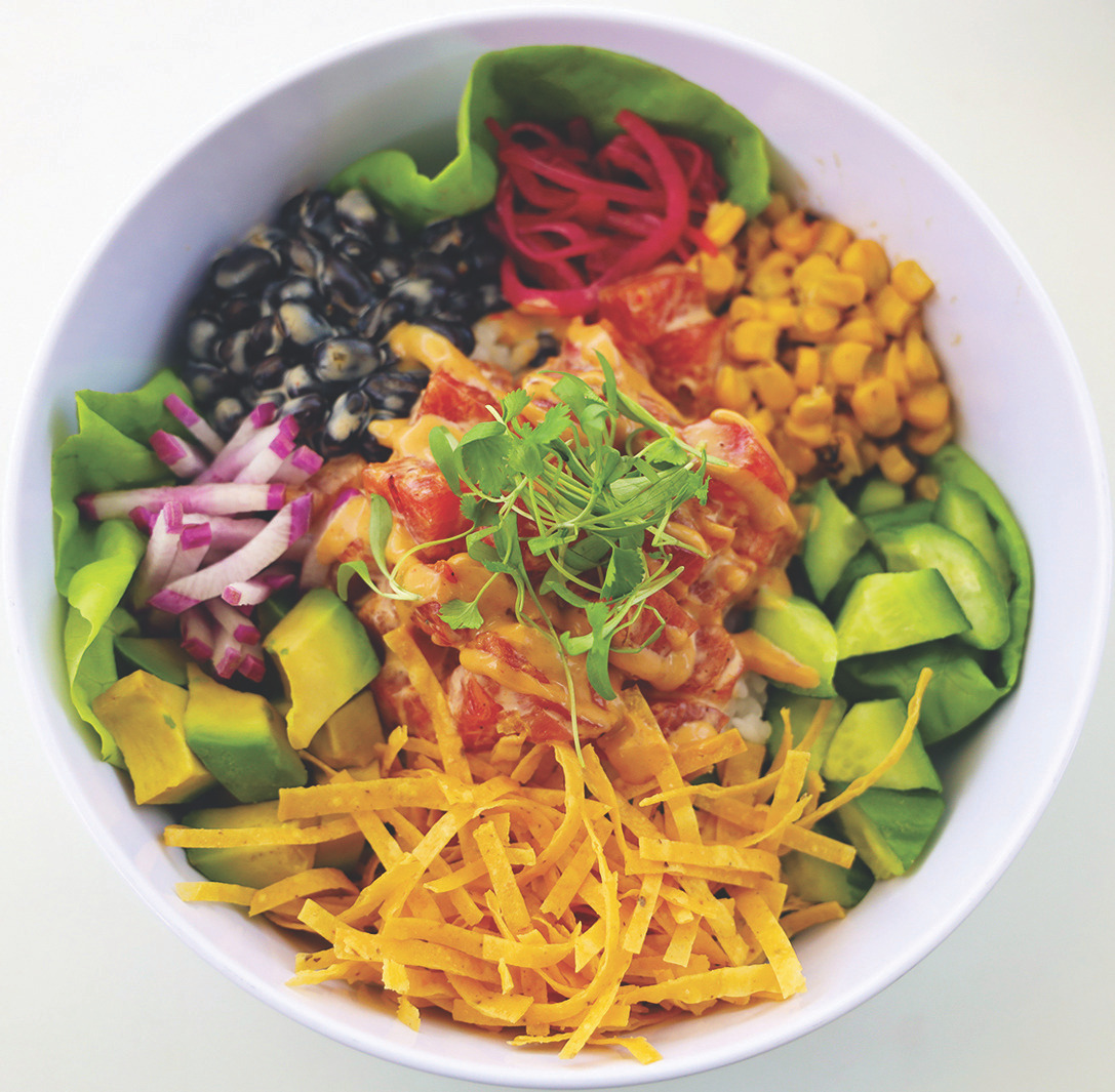Top-down view of a colorful poke bowl with tuna, avocado, corn, black beans, radish and shredded cheese