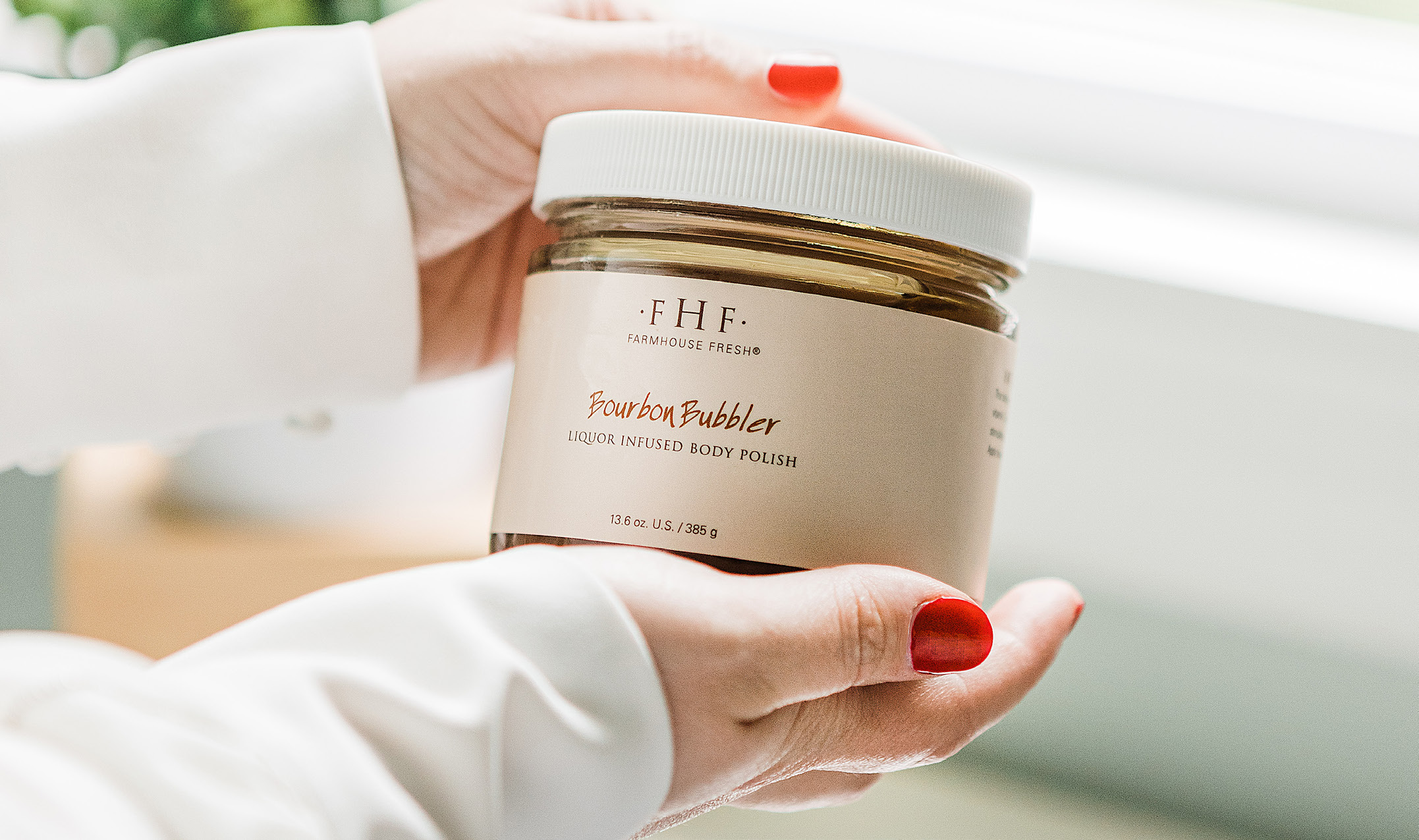 Close up of hands holding a glass jar of Bourbon Bubbler body polish