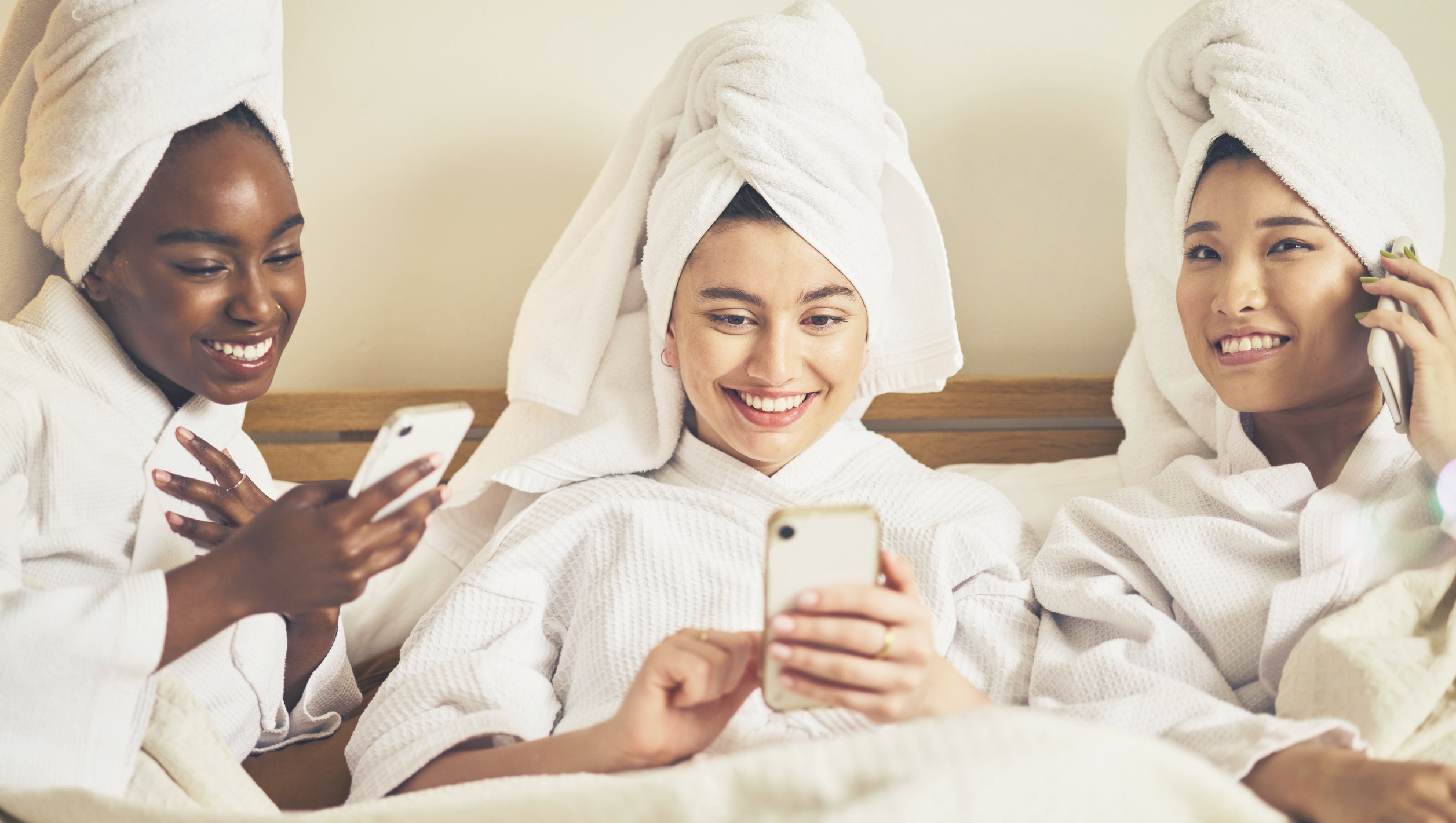 Three young women in spa robes looking at smartphones