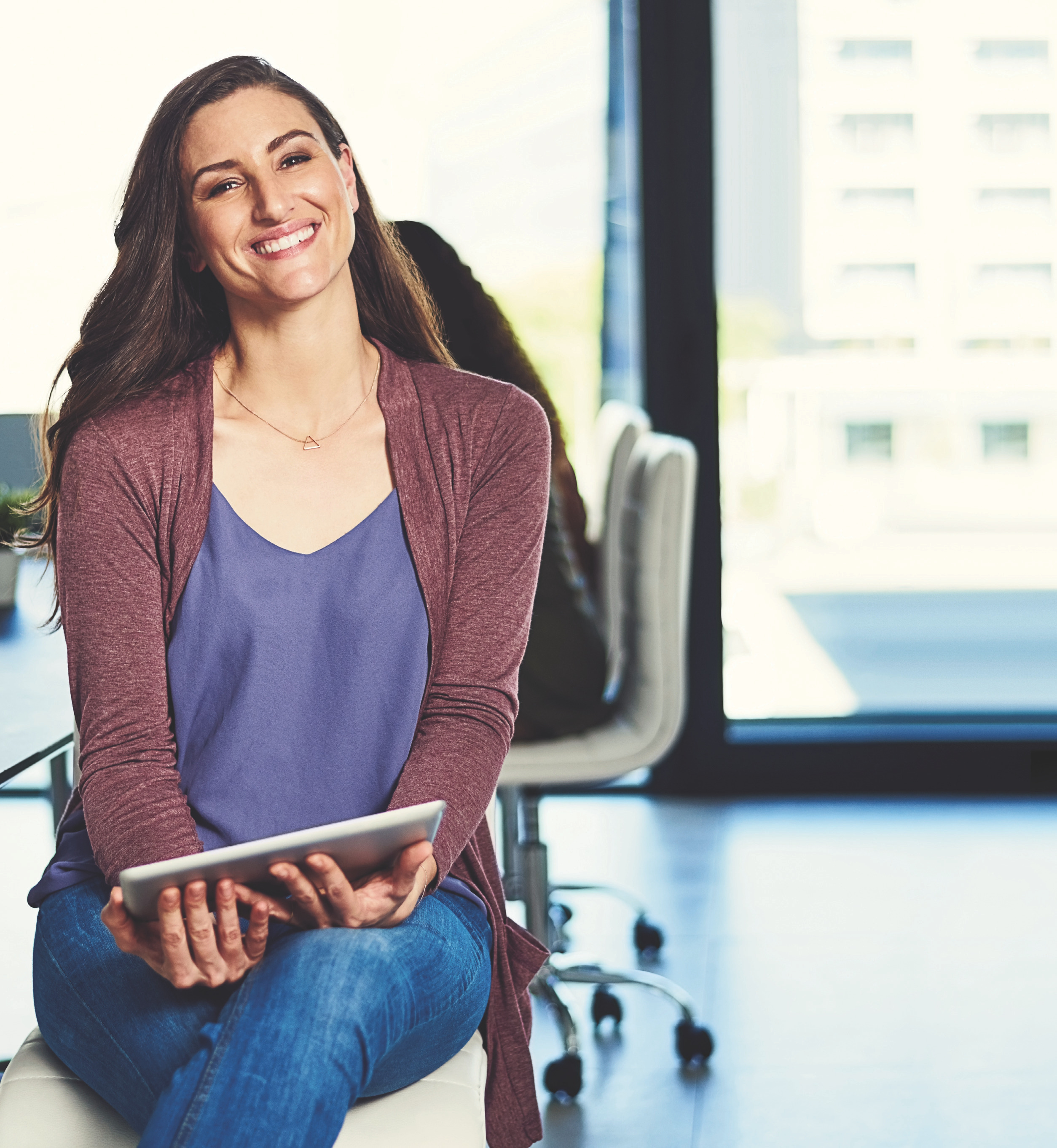 Smiling spa professional seated and holding a tablet in a bright office setting