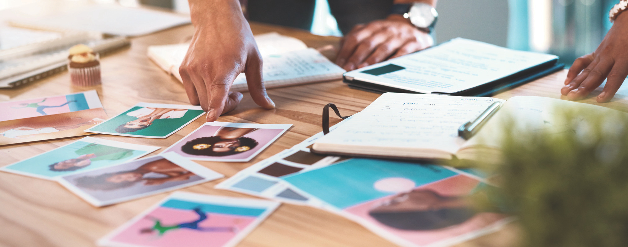 Hands arranging printed photos and swatches on a wooden table