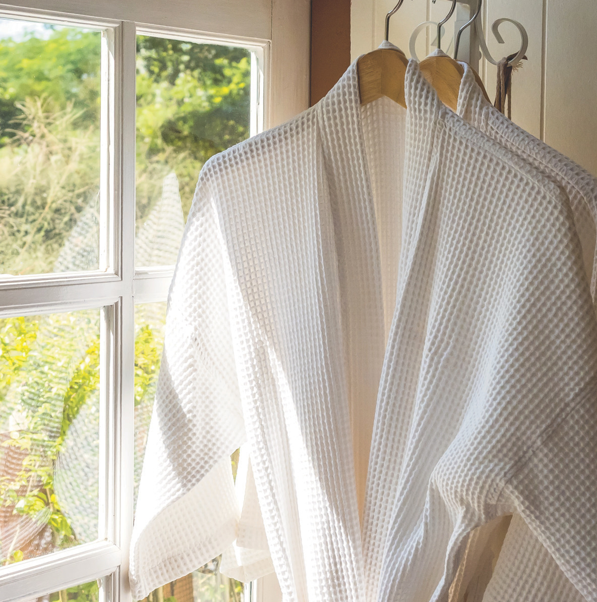 White spa robes hanging by a window.