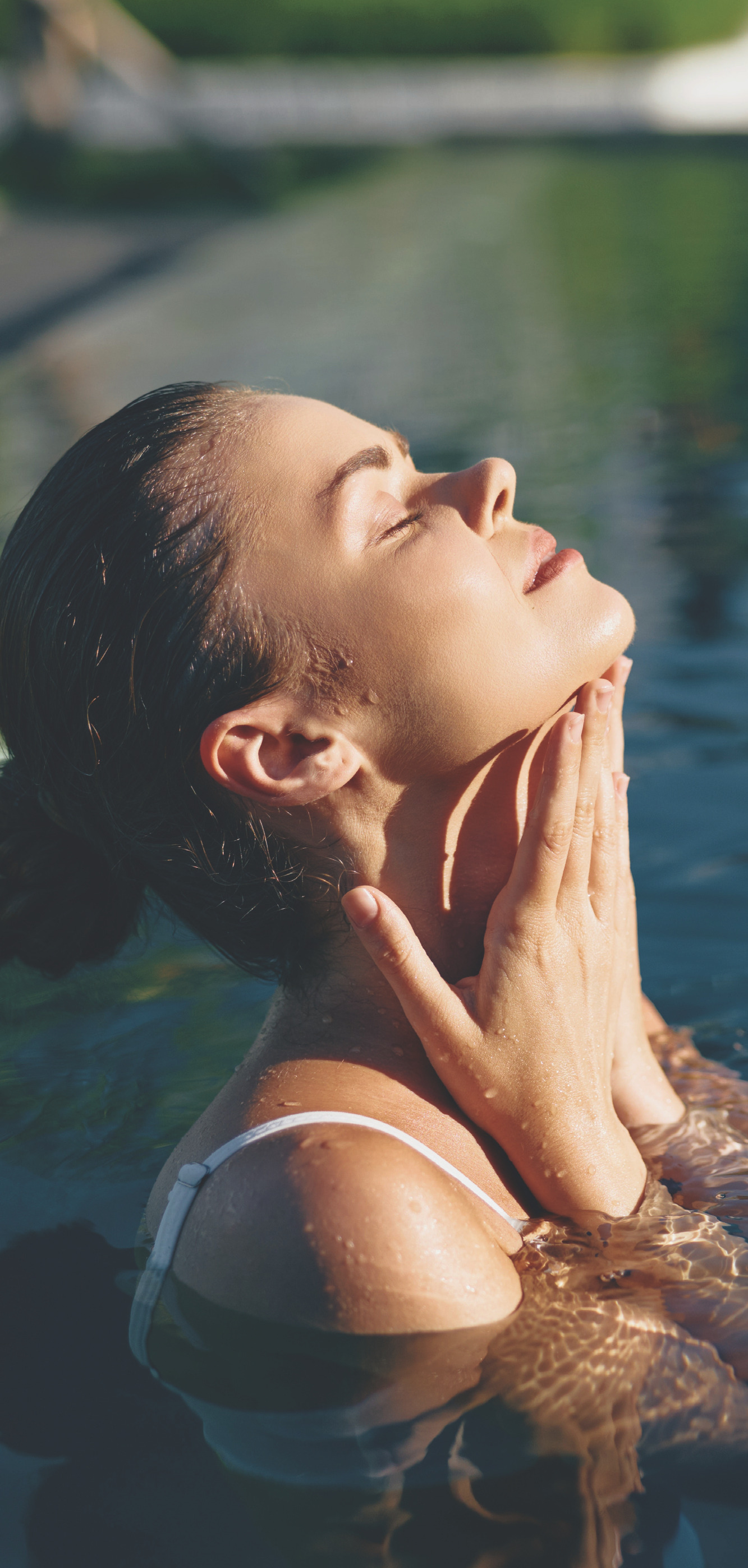 Woman relaxing in a pool with eyes closed, face tilted up toward the sun.