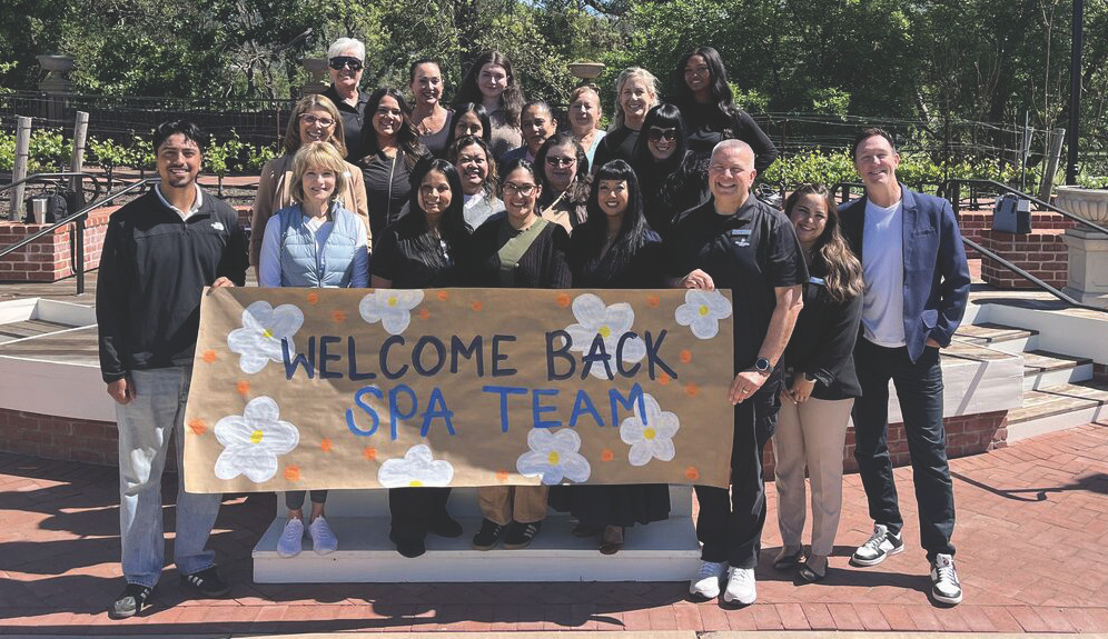 Spa team holding a 'WELCOME BACK SPA TEAM' banner outdoors