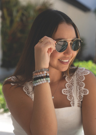 Young woman outdoors wearing sunglasses, smiling while adjusting her glasses.