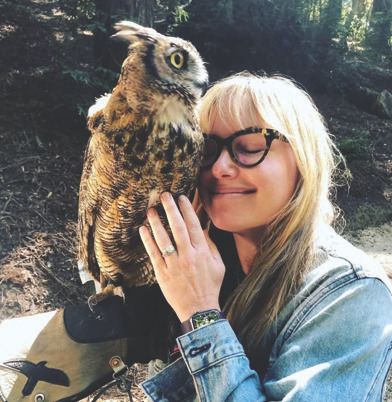 Woman holding and nuzzling a large owl outdoors, smiling