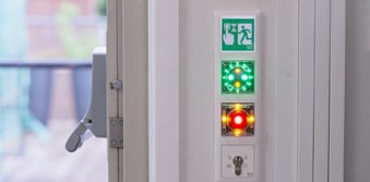 Close-up of an escape door indicator/control panel showing illuminated green and red lights and an emergency exit graphic