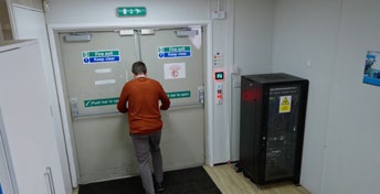 Person in a rust-coloured jumper standing in front of double emergency doors in a back-of-store area