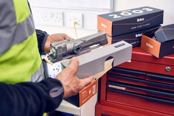Workshop scene showing a technician handling a door closer or hardware component.