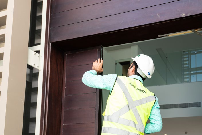 An ASSA ABLOY technician in high-visibility gear inspecting a door installation to ensure compliance and safety.