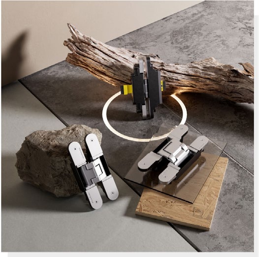 Three metal door hinge components displayed on a studio surface with driftwood and concrete materials