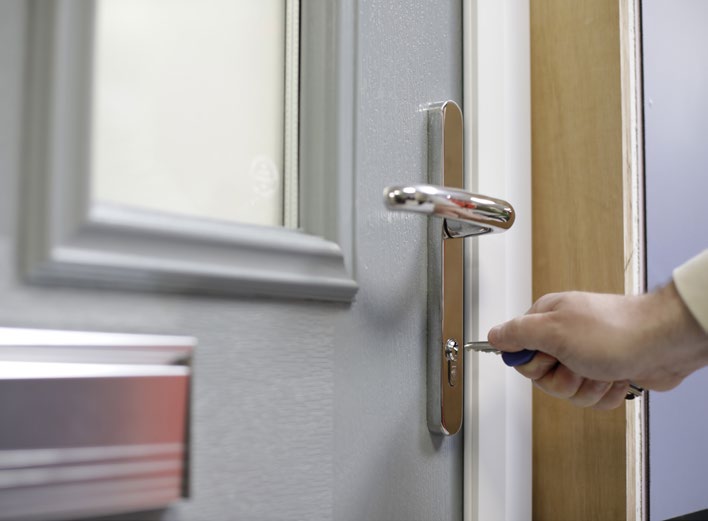 Close-up of a hand holding and turning a key in a door lock.