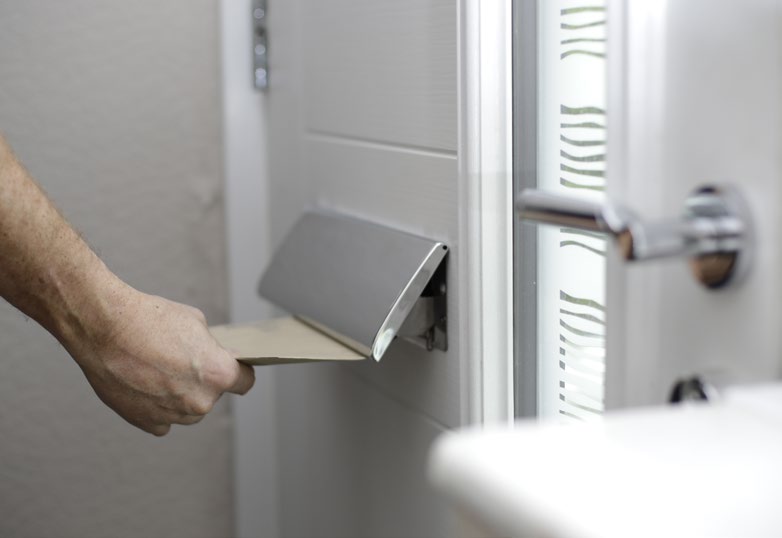Hand inserting a letter into a horizontal TS008 letterplate on a white door.