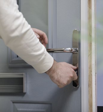 Hand gripping and pushing down a door handle on a grey door.
