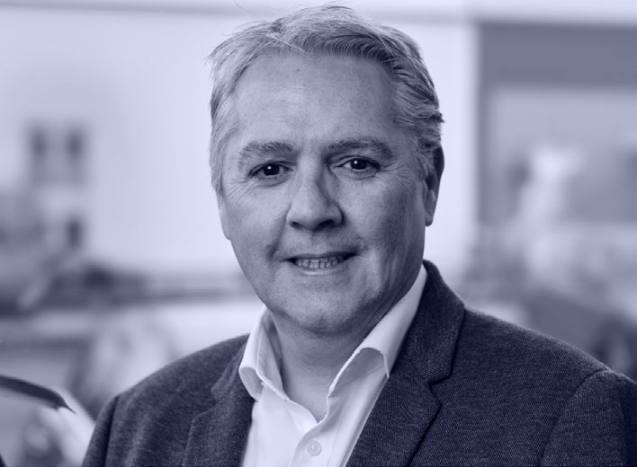 Portrait of Deighton Ridge, Head of Commercial, GfA UK, wearing a suit jacket and white shirt, smiling.