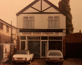 Historic sepia photograph of the original Garage Doors (London) shop-front with two cars parked outside.