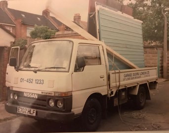 Vintage flatbed truck carrying a garage door panel, an historic company vehicle.