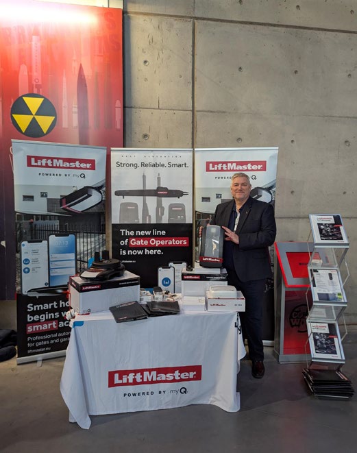 LiftMaster exhibition stand with table, product displays and a representative standing beside banners.