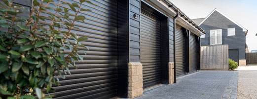 Three adjacent black roller garage doors on contemporary homes, viewed along a driveway.