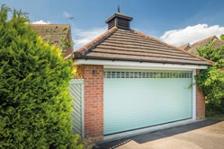 Detached garage with a mint green roller door in a suburban setting, framed by shrubs.