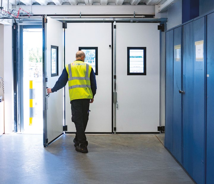 Technician in high-visibility vest operating a large white Swift folding bay door from the interior