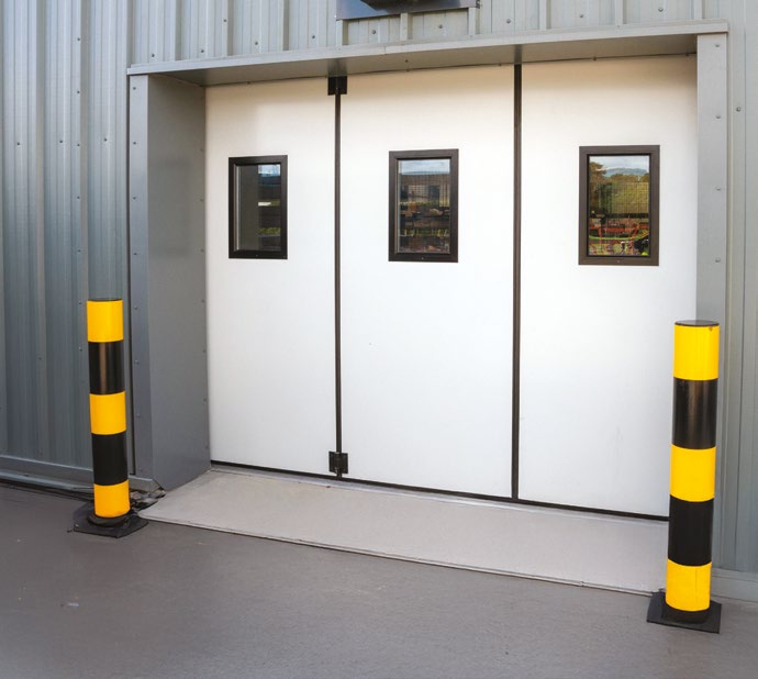 Closed three-panel white industrial door with small viewing windows and safety bollards