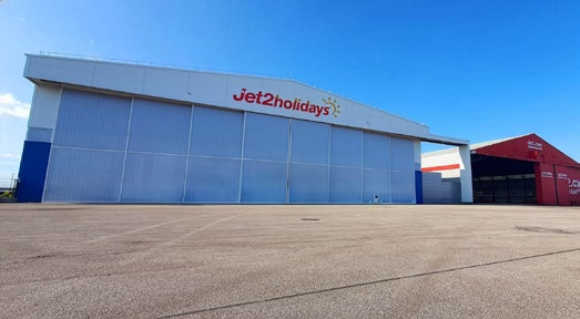 Exterior of a large white aircraft hangar with a blue/grey door and the Jet2holidays logo above the door