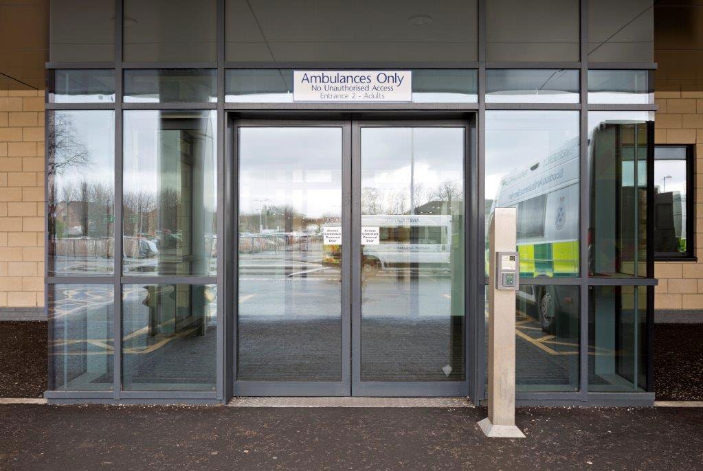 Automatic sliding entrance doors at Queen Elizabeth University Hospital with 'Ambulances Only' sign visible.