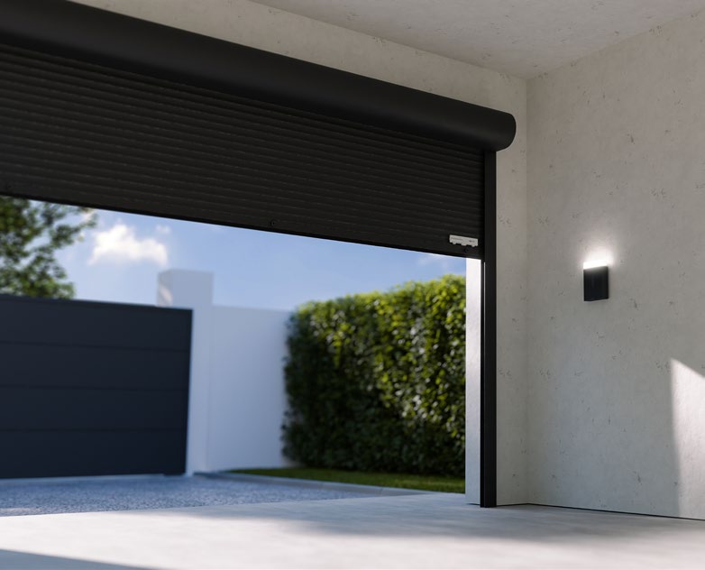 Interior view of a modern garage with roller door partially open, showing driveway and hedge outside