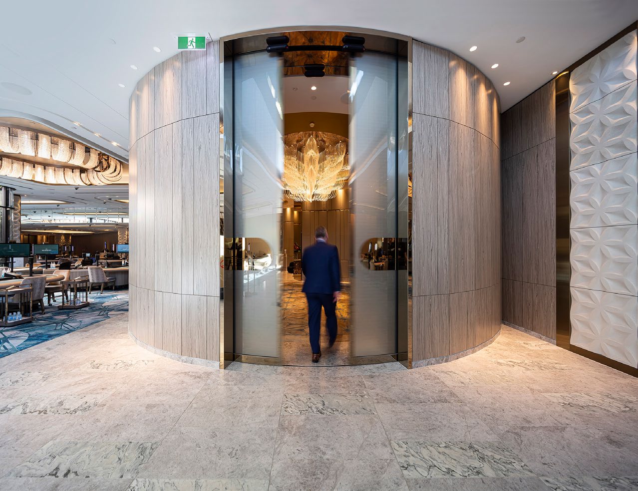 Entrance lobby with automatic glass doors and chandelier, person walking through into a brightly lit reception area.