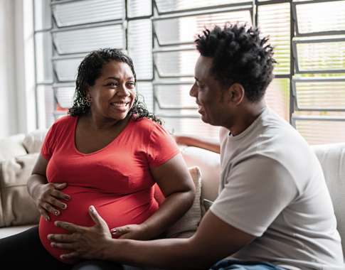 A man and a pregnant woman sitting together, sharing a supportive and smiling moment.