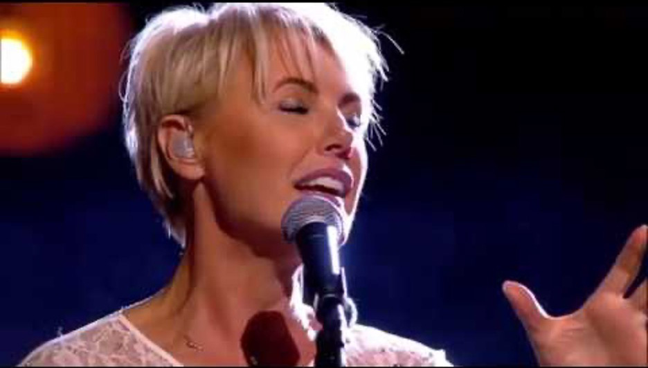 Dana Winner singing into a microphone with eyes closed, expressive hand raised