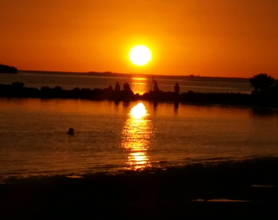 Sunset over water with silhouettes on the shore