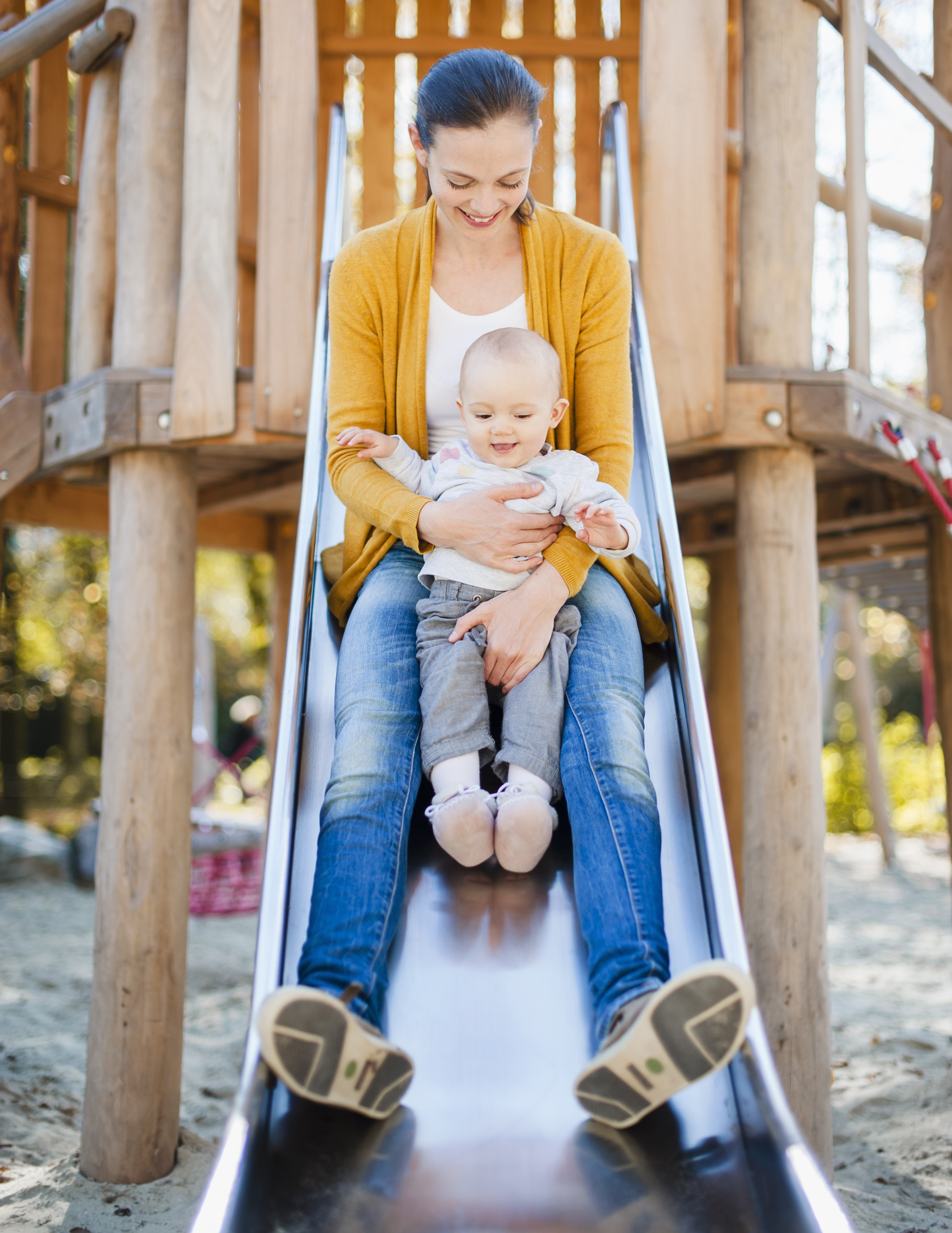 Mother and baby sliding down a playground slide together